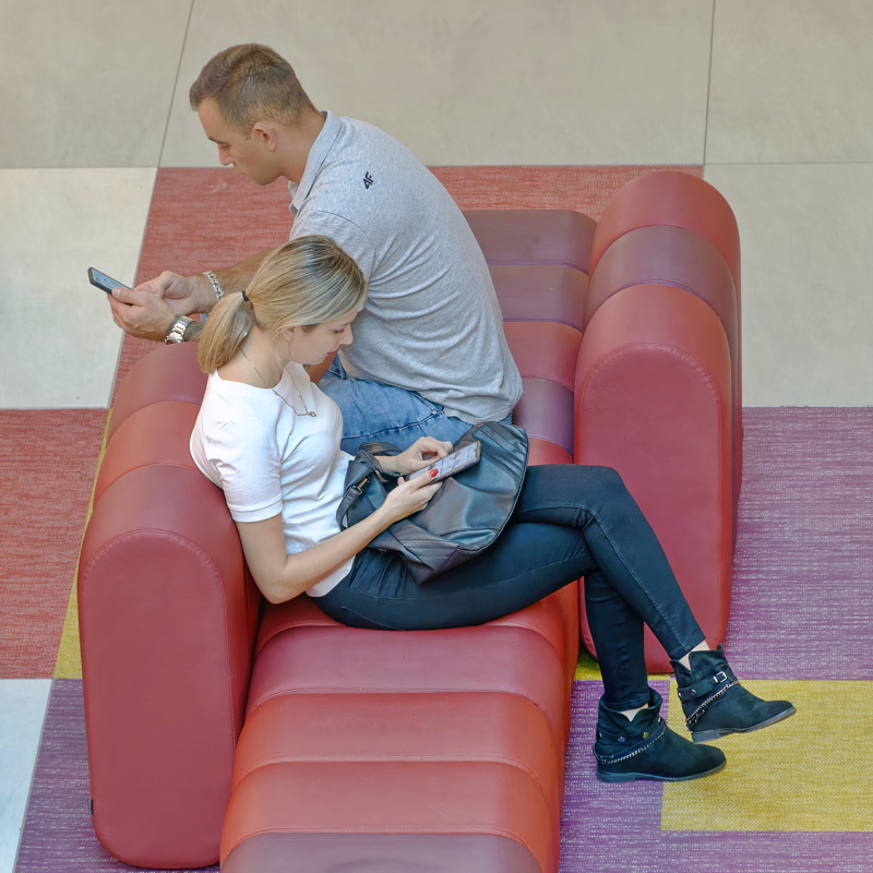 29 - Two individuals seated on a red modular couch while using their mobile devices